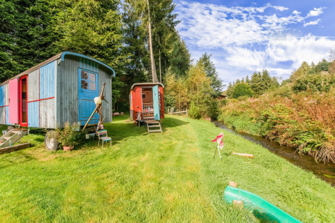 Les Roulottes de Vio: Colorful mobile homes on grassy lawn by a creek, surrounded by trees and blue sky.