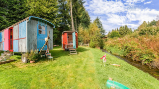 Les Roulottes de Vio: Casas rodantes coloridas en césped junto a un arroyo y rodeadas de árboles y cielo azul.