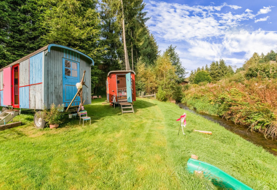 Les Roulottes de Vio: Colorful mobile homes on grassy lawn by a creek, surrounded by trees and blue sky.