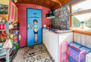 Colorful kitchen inside the mobile home 'Les Roulottes de Vio' with retro decor and countryside views in Belgium.