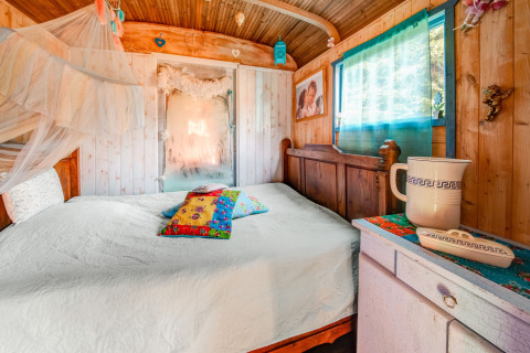 Cozy bedroom inside a mobile home at Les Roulottes de Vio in Belgium, featuring wood decor and bright cushions.
