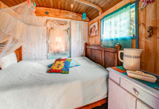 Cozy bedroom inside a mobile home at Les Roulottes de Vio in Belgium, featuring wood decor and bright cushions.