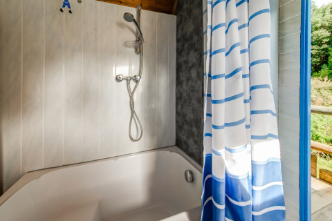 Bathroom in mobile home with bathtub, shower head, and blue-striped curtain at Les Roulottes de Vio, Belgium.