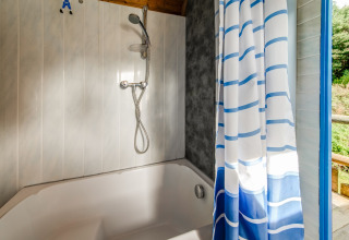Bathroom in mobile home with bathtub, shower head, and blue-striped curtain at Les Roulottes de Vio, Belgium.