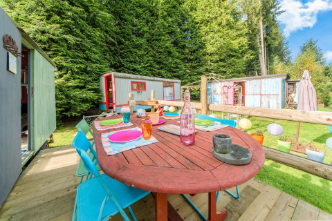 Colorful outdoor dining area at Les Roulottes de Vio mobile home, surrounded by trees and wagons in Belgium.