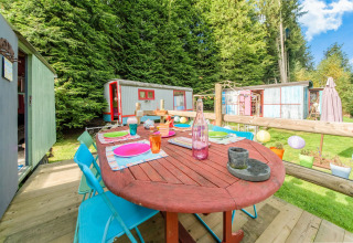 Colorful outdoor dining area at Les Roulottes de Vio mobile home, surrounded by trees and wagons in Belgium.