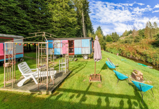 Les Roulottes de Vio mobile home in Belgium, with colorful wagons, deck chairs, and meadow seating area.