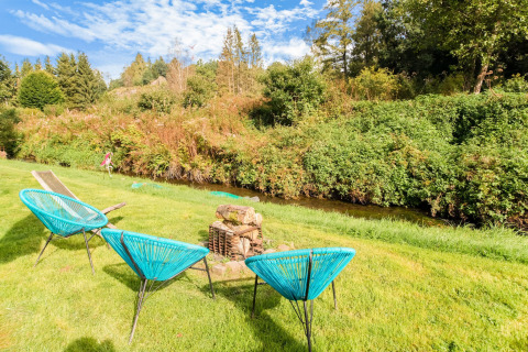 Outdoor setting at Les Roulottes de Vio in Belgium with blue chairs by a stream and lush greenery.
