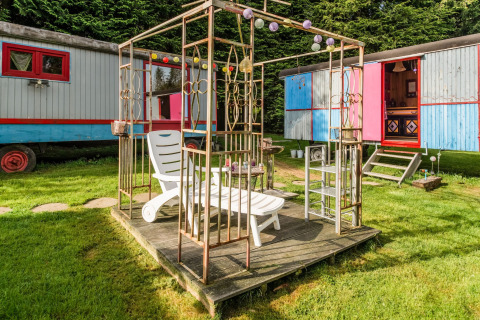 Outdoor lounge area with sunbed near colorful mobile homes at Les Roulottes de Vio, Belgium.