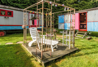 Outdoor lounge area with sunbed near colorful mobile homes at Les Roulottes de Vio, Belgium.