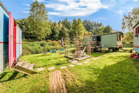 Colorful mobile homes and playground at Les Roulottes de Vio in Belgium, surrounded by lush greenery.