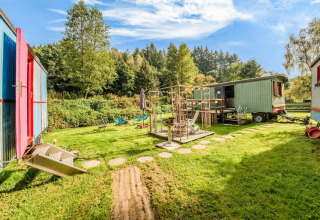 Colorful mobile homes and playground at Les Roulottes de Vio in Belgium, surrounded by lush greenery.