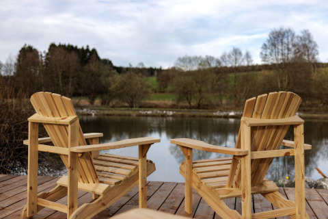 Twee houten stoelen op een terras aan het meer met uitzicht op een rustige rivier en natuur.