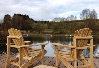 Twee houten stoelen op een terras aan het meer met uitzicht op een rustige rivier en natuur.