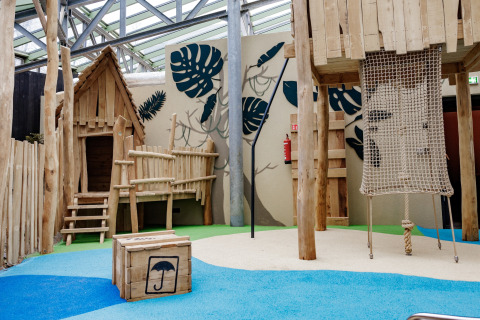 Speelplaats met houten hutten en klimnet bij een kleurrijke glampingaccommodatie voor kinderen.