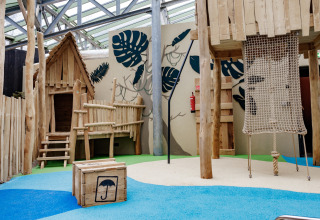 Speelplaats met houten hutten en klimnet bij een kleurrijke glampingaccommodatie voor kinderen.