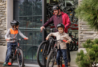 Gezin met helmen maakt zich klaar voor een fietstocht bij een glamping-accommodatie met fietsen zichtbaar.