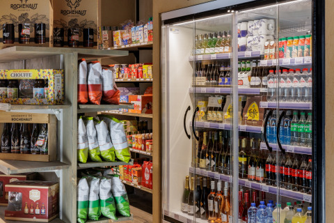 Kleine supermarkt bij een glamping met chips, snacks, frisdrank, wijn en bier in schappen en een koelkast.