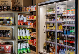 Kleine supermarkt bij een glamping met chips, snacks, frisdrank, wijn en bier in schappen en een koelkast.