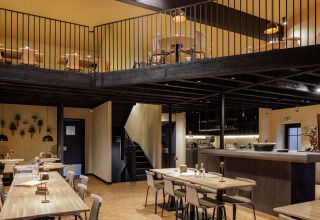 Interieurfoto van een gezellig restaurant met houten tafels en entresol bij een glamping-accommodatie.