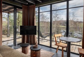 Moderne woonkamer in Hillview Resort Grandvoir 1, België, met panoramisch boszicht door grote ramen.