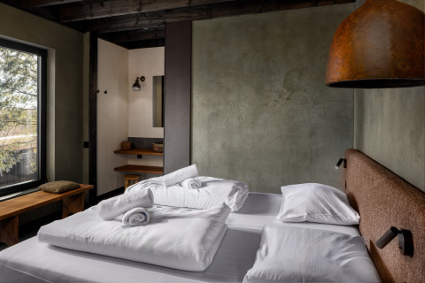 Moderne slaapkamer met tweepersoonsbed, rustieke muren en groot raam in Hillview Resort Grandvoir 1, België.
