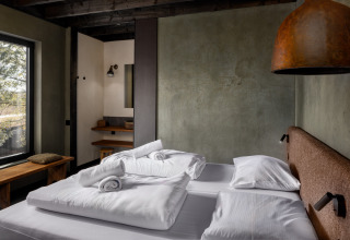 Moderne slaapkamer met tweepersoonsbed, rustieke muren en groot raam in Hillview Resort Grandvoir 1, België.