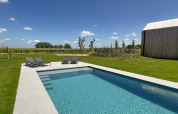 Piscina moderna y tumbonas en la cabaña 'Natural Escape' en Bélgica, rodeada de naturaleza y cielo azul.