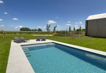 Piscina moderna y tumbonas en la cabaña 'Natural Escape' en Bélgica, rodeada de naturaleza y cielo azul.