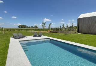 Moderne pool ved hytten 'Natural Escape' i Belgien, omgivet af grønne marker og klart himmelvejr.