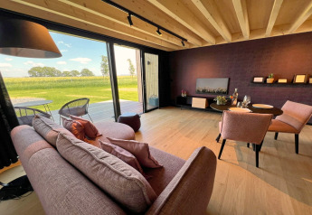 Acogedora sala de la cabaña 'Natural Escape' en Bélgica con vistas a extensos campos verdes.
