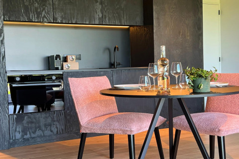 Moderne køkken og spiseplads i en hytte ved navn 'Natural Escape' i Belgien, med lyserøde stole og vinflaske.