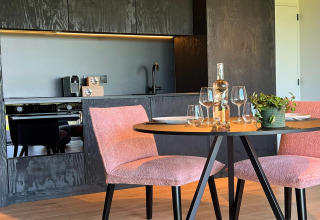 Moderne køkken og spiseplads i en hytte ved navn 'Natural Escape' i Belgien, med lyserøde stole og vinflaske.