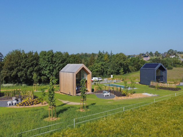 Luchtfoto van twee moderne hutten bij Natural Escape, omringd door groene velden, bomen en paden.