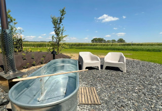 Udendørs område ved 'Natural Escape' i Belgien med to stole, en metalbadekar og grønne marker.