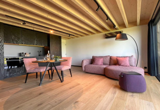 Moderne stue i hytten 'Natural Escape' i Belgien med træloft, lilla sofa og åben køkken.