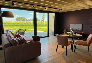 Lys stue i en hytte ved navn 'Natural Escape' i Belgien med udsigt til grønne marker gennem store vinduer.