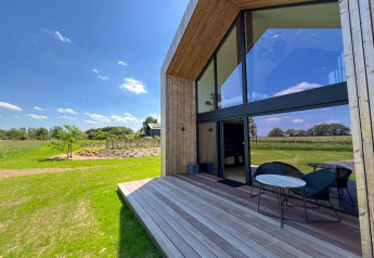 Vista soleada de la terraza de la cabaña 'Natural Escape' en Bélgica, rodeada de campo verde.
