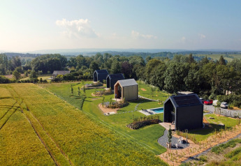 Vista aérea de cabañas modernas en Natural Escape, Bélgica, rodeadas de campos y bosque bajo cielo despejado.