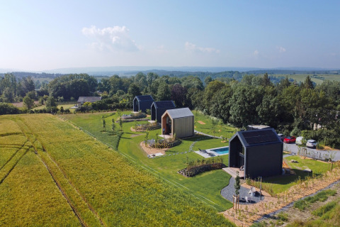 Luftfoto af moderne hytter ved Natural Escape i Belgien, omgivet af marker og skov på en solrig dag.