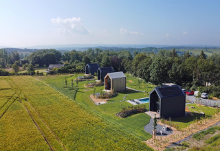 Luftfoto af moderne hytter ved Natural Escape i Belgien, omgivet af marker og skov på en solrig dag.