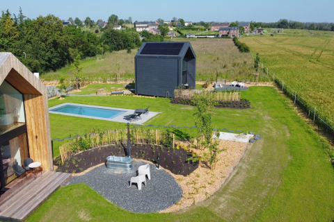 Luftfoto af Natural Escape kabine i Belgien med pool, terrasse, have og grønne marker i baggrunden.