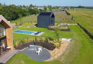 Luftfoto af Natural Escape kabine i Belgien med pool, terrasse, have og grønne marker i baggrunden.