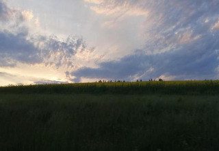 Solnedgang over et grønt landskab set fra Natural Escape-hytten i Belgien, dramatiske skyer i himlen.