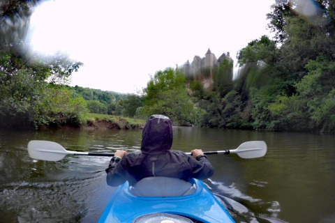 Person i kajak på en flod nær grønne træer og en sløret bygning, taget ved Natural Escape i Belgien.