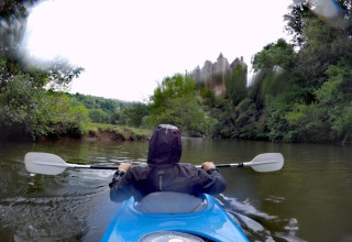 Person i kajak på en flod nær grønne træer og en sløret bygning, taget ved Natural Escape i Belgien.