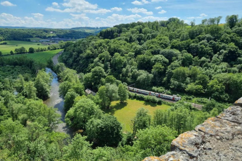 Udsigt over frodige grønne bakker, en flod og et tog, set fra hytten Natural Escape i Belgien.