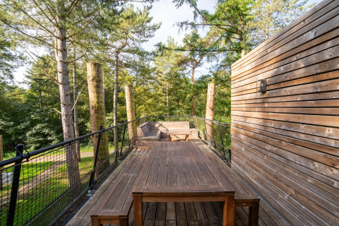 Udendørs terrasse ved The TreeLoft med træmøbler og smuk udsigt over grønne trætoppe i naturen.