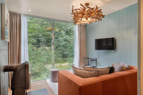 Soggiorno a The TreeLoft by YourNature con vista foresta, divano moderno e lampadario in legno unico.