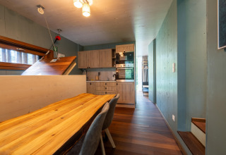 Modern treehouse interior featuring a wooden dining table, kitchen area, and stairs with natural light.